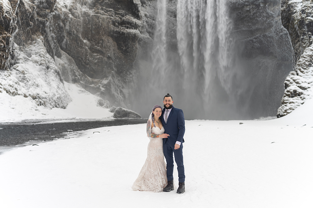 A bride and groom pose in front of a frozen waterfall in Iceland, captured with exceptional clarity and depth by the Tamron 35-150mm F2-2.8—showcasing the lens's versatility for impromptu portraits in extreme conditions during this hands-on review.
