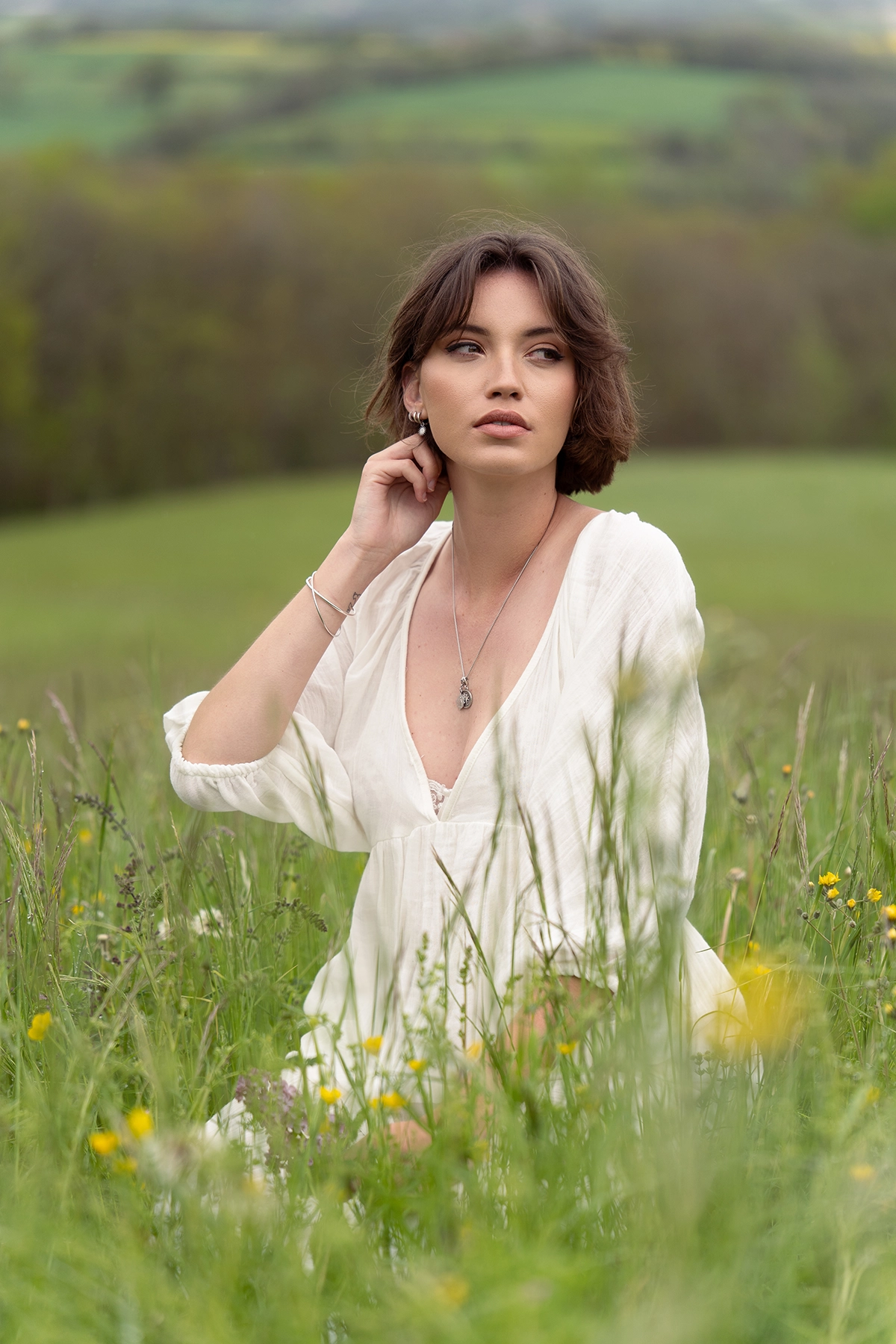 Woman in a white dress sitting in a wildflower meadow, softly lit by natural summer photography lighting in an open field.