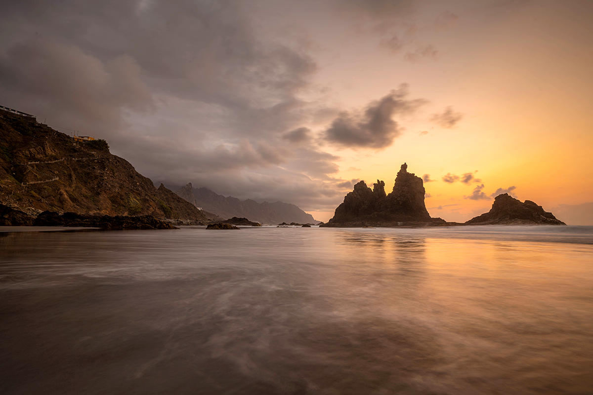 A peaceful shoreline with rock formations rising from the water photographed as the sun is captured using a silky long-exposure photography effect.