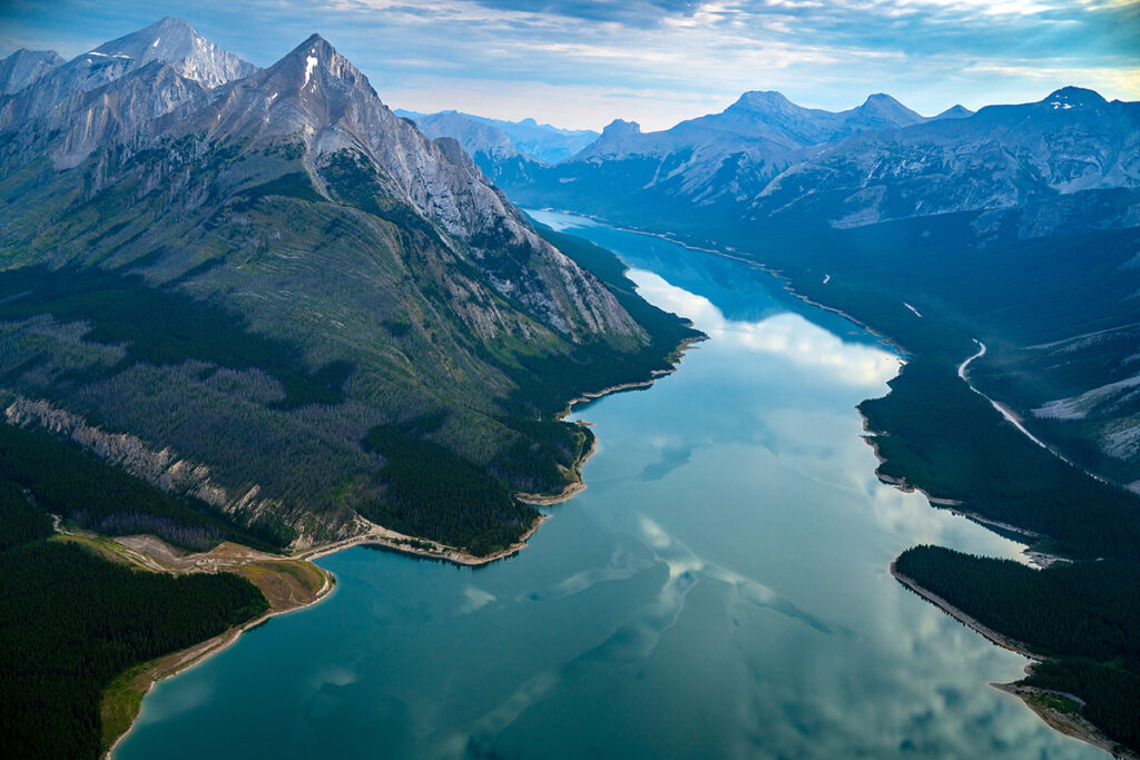 A breathtaking aerial view of a mountain range with a long, winding lake nestled between the peaks, reflecting the sky above.