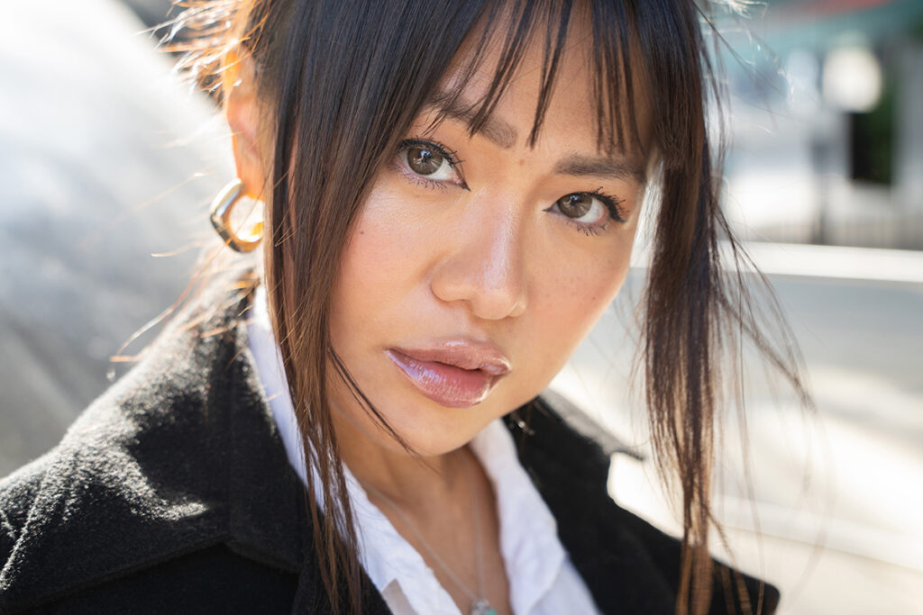 A close-up portrait of a woman with long dark hair gazing directly towards the camera. 