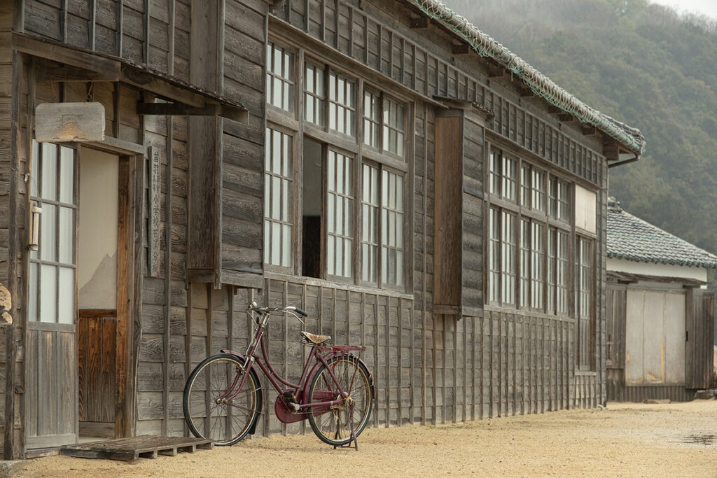 A vintage bicycle leans against the wooden exterior of an old building on a dirt path.