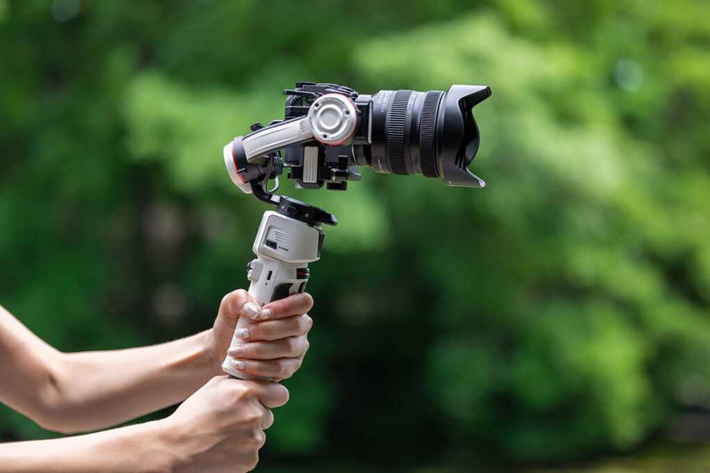 A person holds a professional camera mounted on a handheld gimbal stabilizer.  