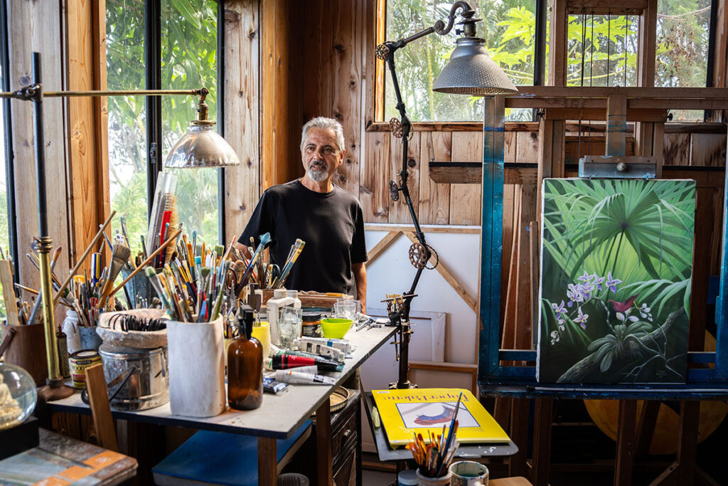 An artist stands in their studio surrounded by painting supplies.