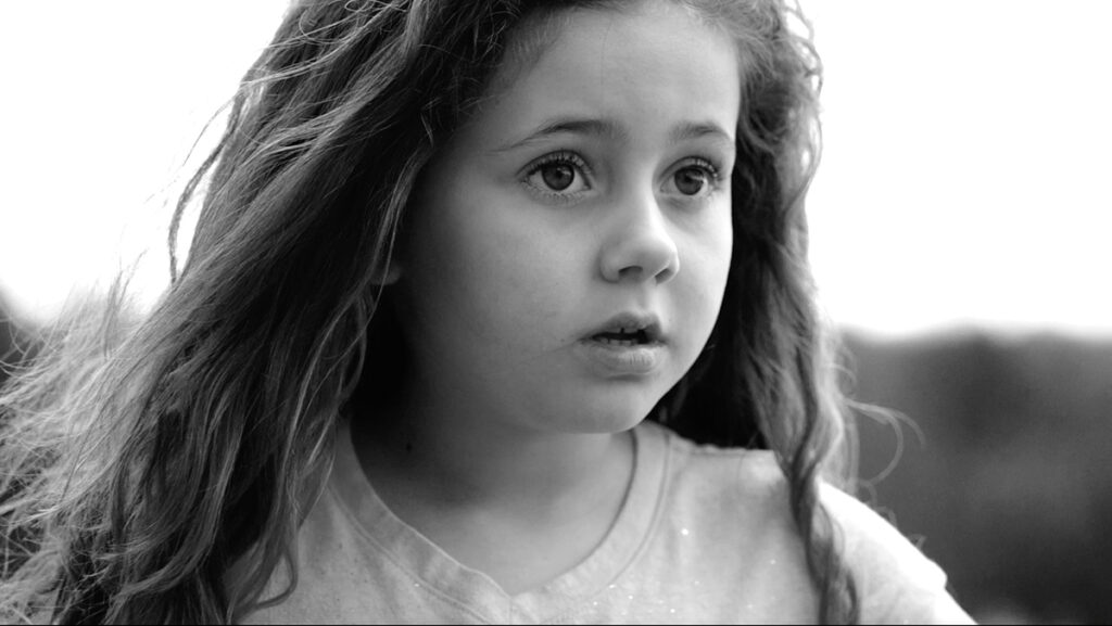 A black and white photograph of a child, with cinematography camera techniques used to blur the background to draw the focus to the child’s face.