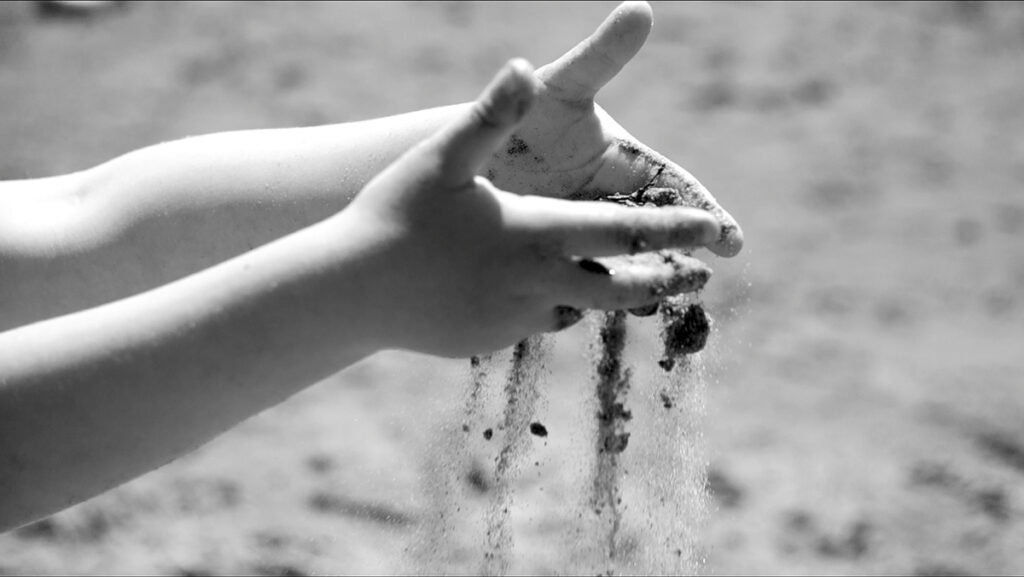 A black and white close-up picture of a child’s hands playing with sand on a beach.