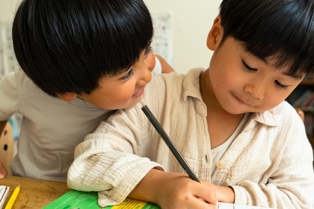 Two young children engaged in an activity at a table with paper and writing utensils. 