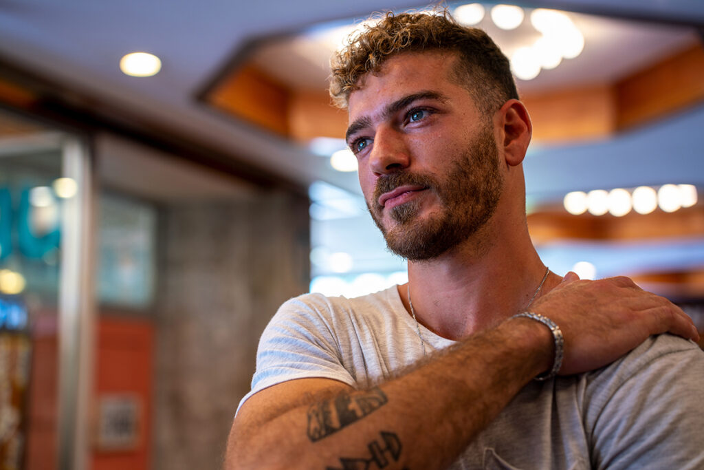 A portrait of a man with short, curly hair and a trimmed beard, looking contemplatively to the side with one hand resting on his shoulder.