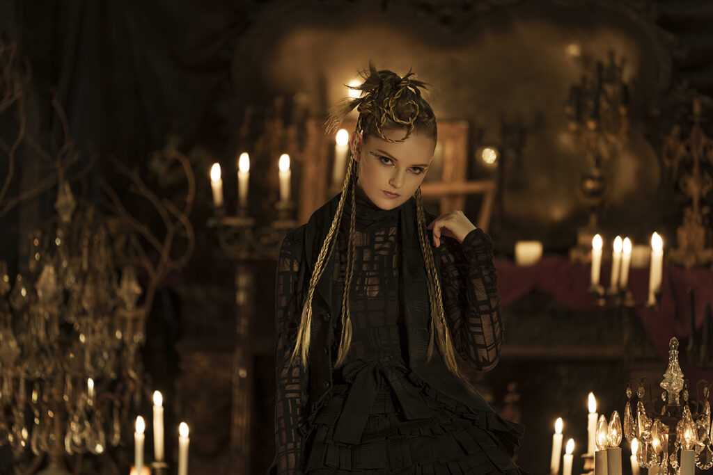 A dramatic portrait of a young woman in a gothic setting lit with candles shot using one of Tamron’s best camera lenses for portrait photography. 