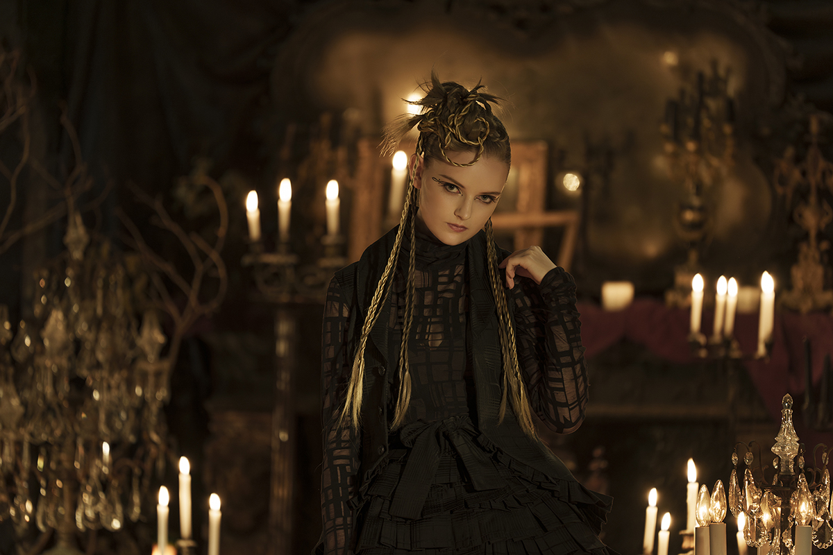 A dramatic portrait of a young woman in a gothic setting lit with candles shot using one of Tamron’s best camera lenses for portrait photography.