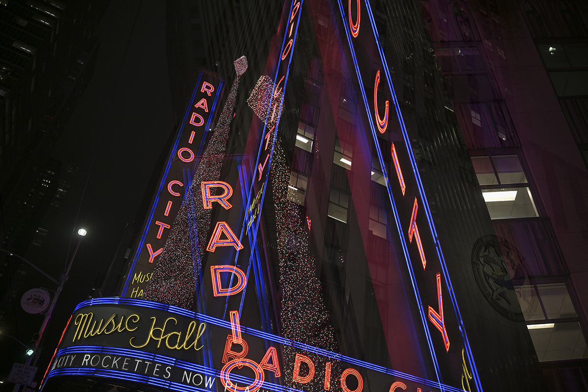 Uma exposição múltipla das icônicas luzes de neon do Radio City Music Hall brilham vibrantemente contra o céu escuro da noite.