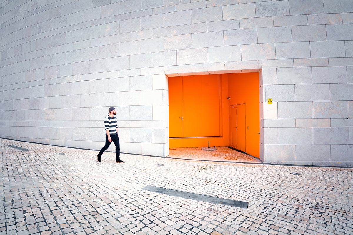 Un homme passant devant une porte de couleur orange.