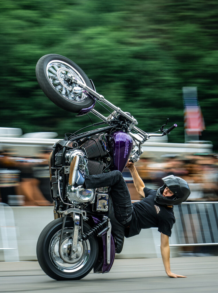 Un tipo haciendo un caballito en una moto morada.