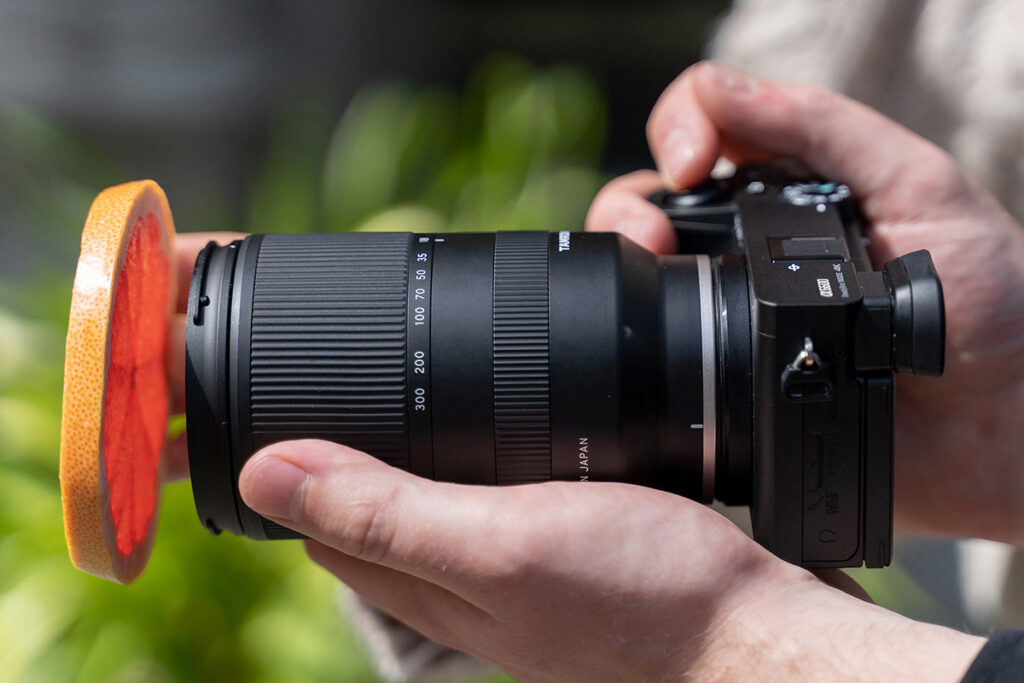 A close-up of hands holding a camera with a slice of a citrus fruit positioned in front of the lens.