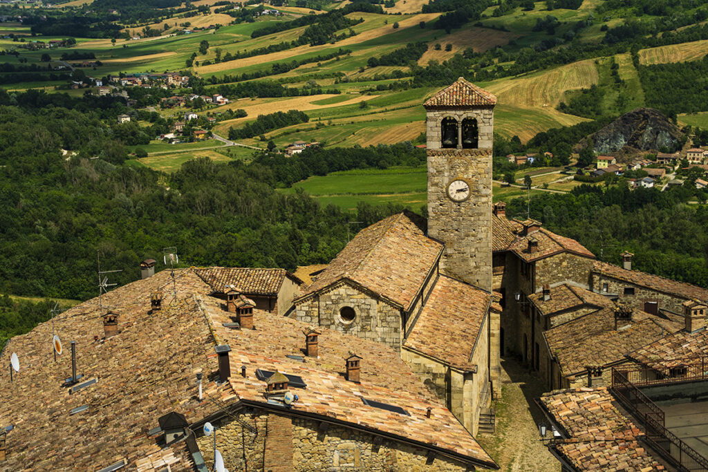 Una vista panorámica de un pueblo histórico con tejados de terracota y una torre de reloj de piedra, rodeado de ondulantes colinas verdes tomada con uno de los mejores objetivos para montura en E de Sony.