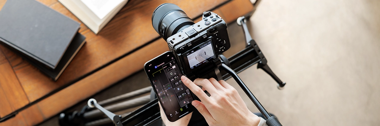 Fotógrafo usando o aplicativo móvel TAMRON Lens Utility™ Ver. 5.0 para controlar o foco e as configurações da lente durante uma filmagem com câmera em um controle deslizante motorizado.