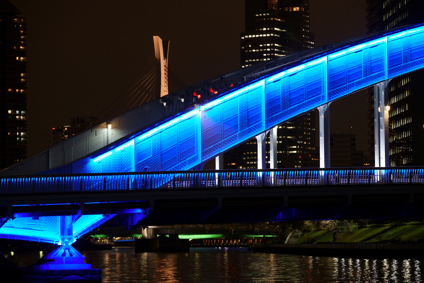 Un pont moderne éclairé de nuit par des lumières bleues vibrantes, avec pour toile de fond la ligne d'horizon d'une ville.