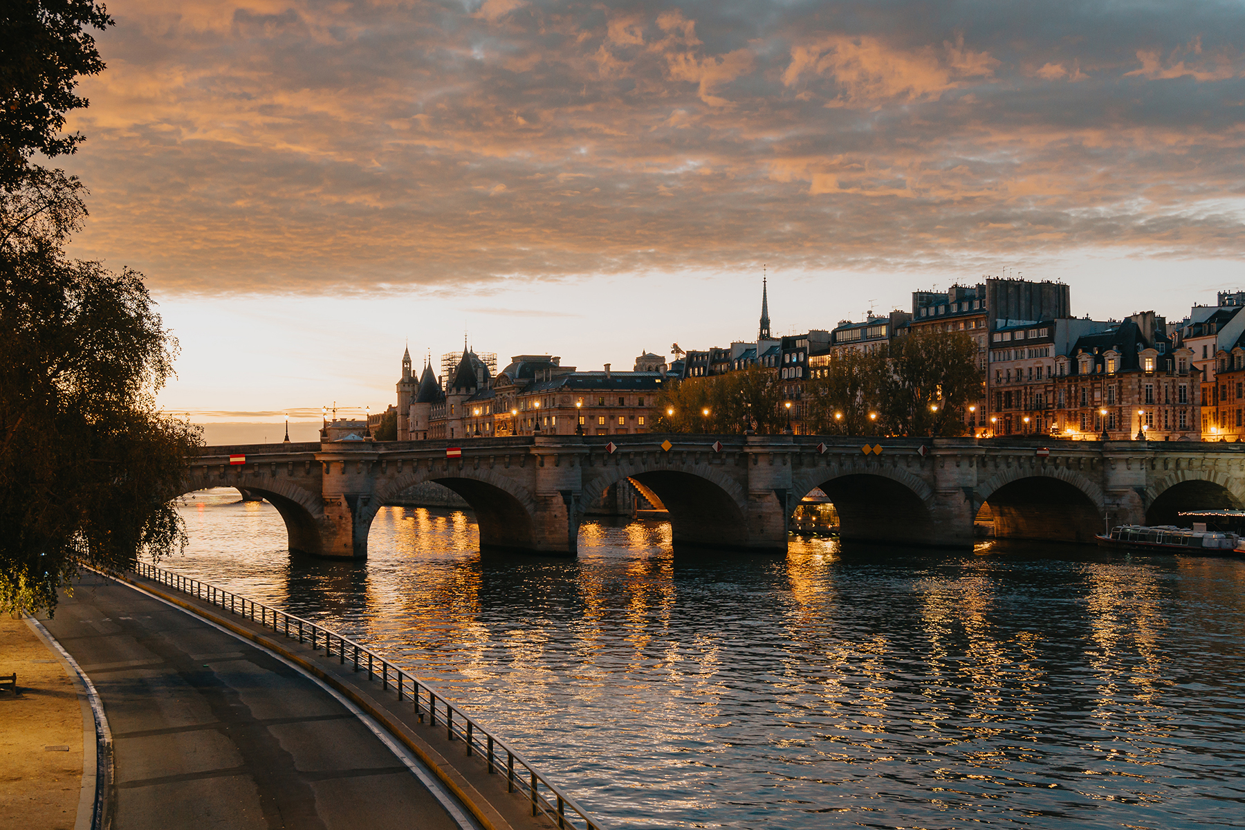 Une vue sereine d'un pont éclairé et de bâtiments historiques se reflétant sur une rivière calme au crépuscule.