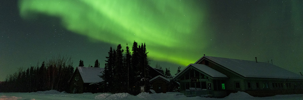 Des aurores boréales époustouflantes au-dessus de cabanes enneigées sous un ciel étoilé.
