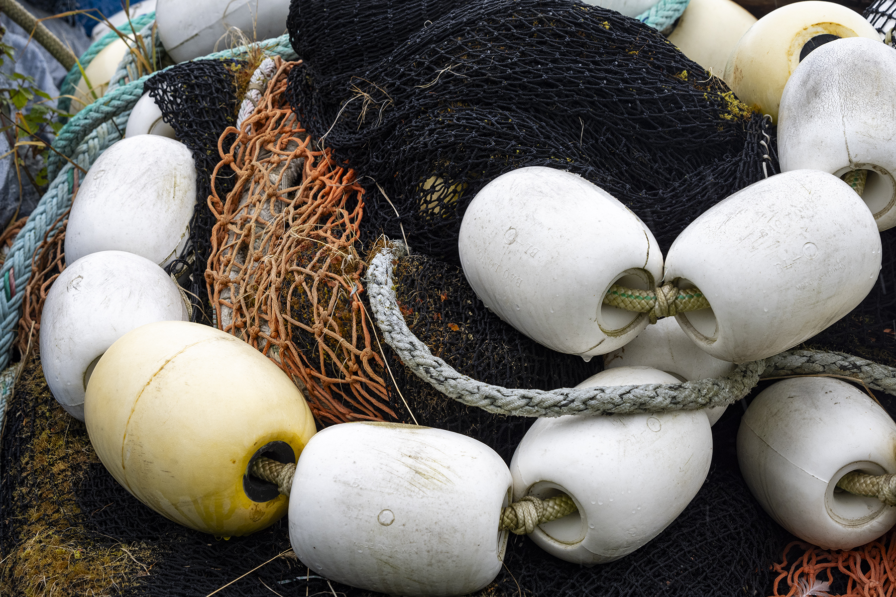 Une pile de matériel de pêche, comprenant des filets, des cordes et des bouées blanches, présentant une texture robuste et bien utilisée.