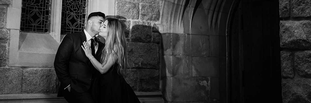 A romantic black-and-white editorial style wedding photography portrait of a couple embracing in front of an elegant stone architecture, exuding timeless sophistication and cinematic allure.