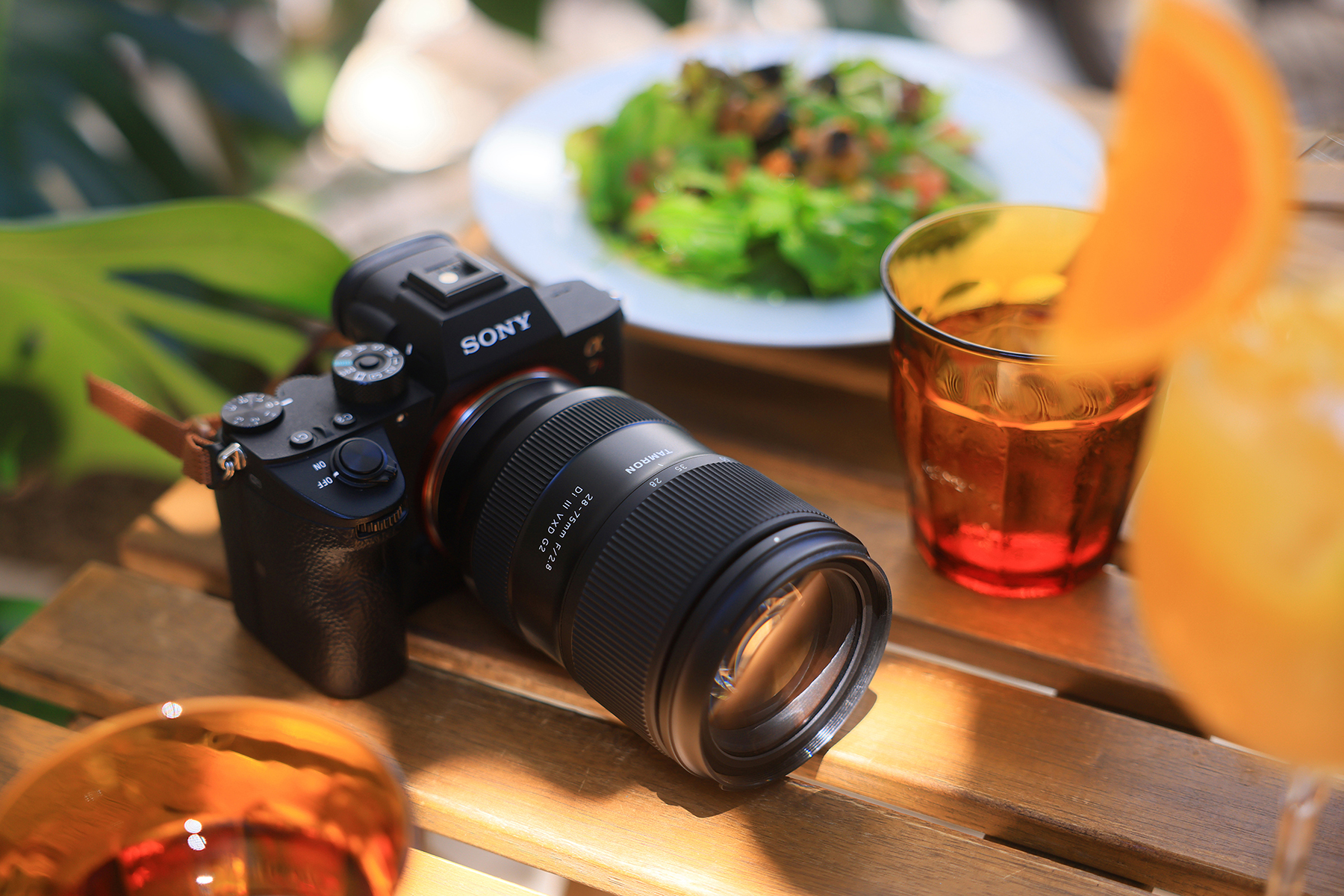 Lente Tamron 28-75 mm G2 em uma câmera sem espelho cercada por bebidas vibrantes e vegetação fresca, mostrando a criatividade em cada detalhe dessa imagem com luz natural.