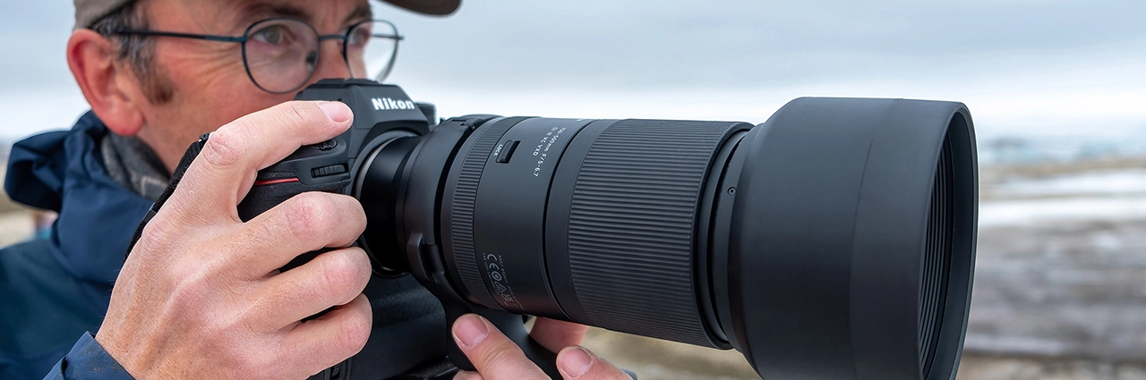 Fotógrafo usando uma câmera mirrorless Nikon com uma lente zoom teleobjetiva TAMRON ao ar livre em uma paisagem de inverno.