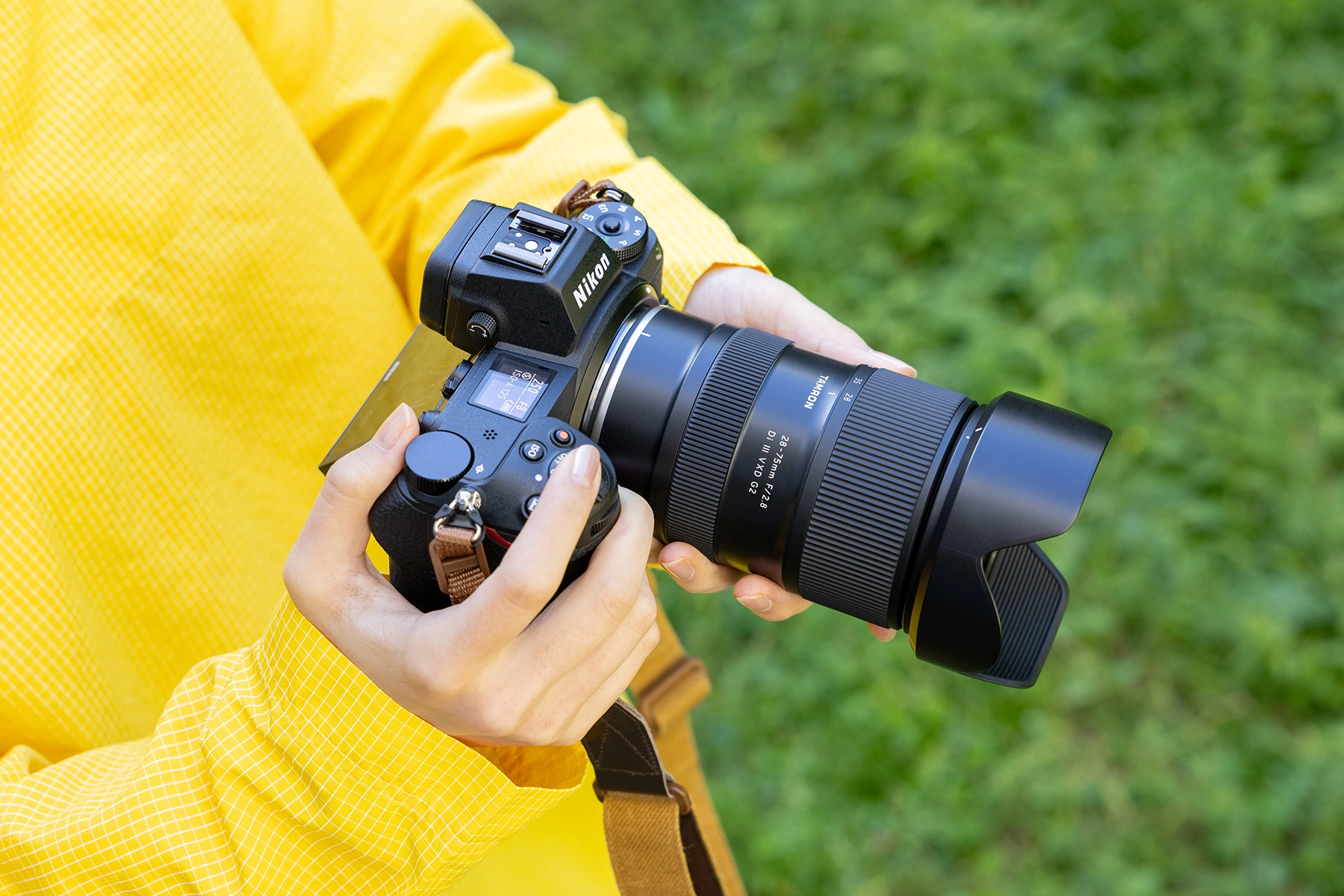 Fotógrafo con una cámara sin espejo Nikon serie Z y un objetivo compacto y ligero TAMRON 28-75 mm F/2,8, listo para disparar en un entorno verde al aire libre.