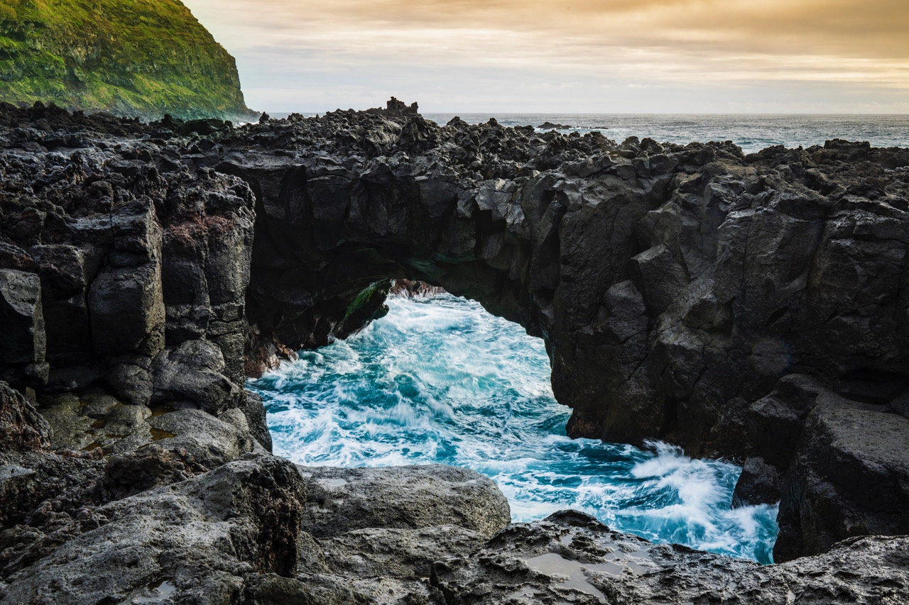 Dramático arco marino rocoso con olas rompiendo en una escarpada costa al atardecer, fotografiado con un objetivo de montura TAMRON Z a una distancia focal gran angular.