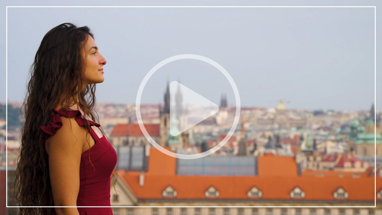 Video thumbnail featuring a woman in a red dress enjoying a scenic city view with historic architecture in the background.