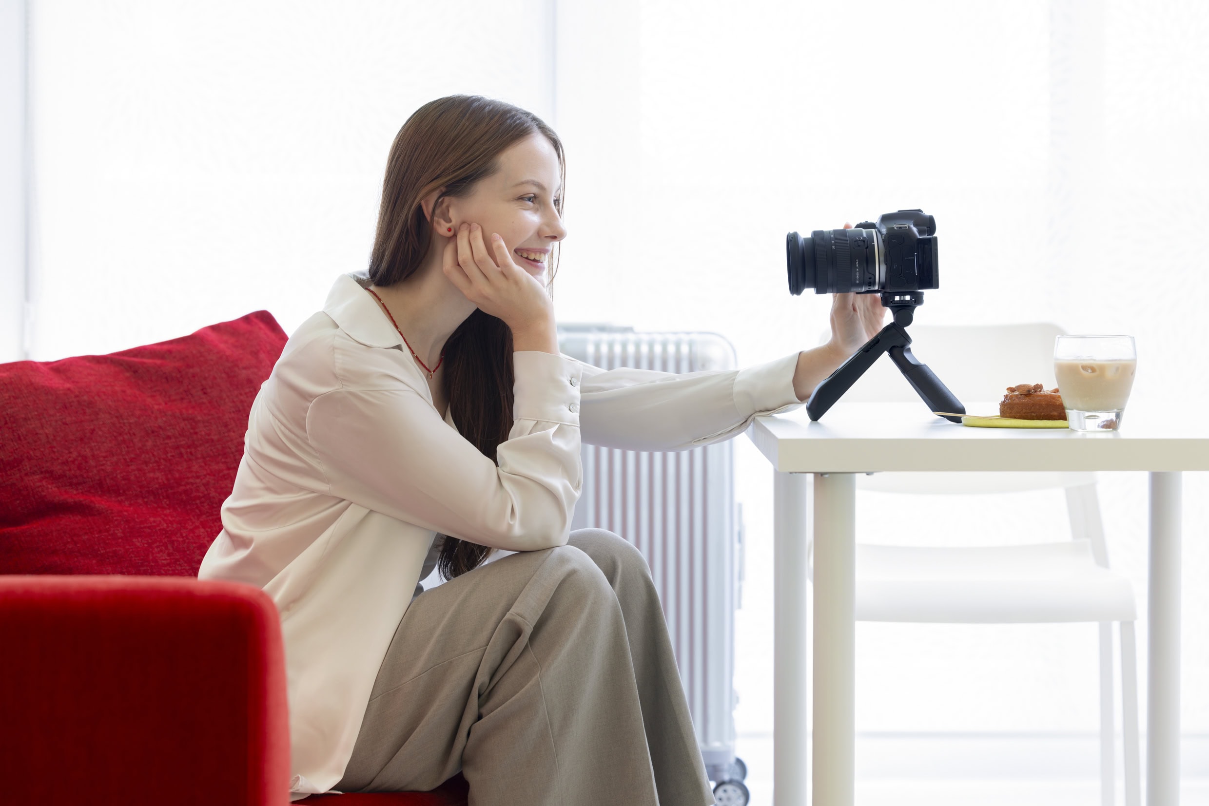 Woman filming a lifestyle vlog indoors using a mirrorless camera with a Tamron wide-angle lens mounted on a tabletop tripod.