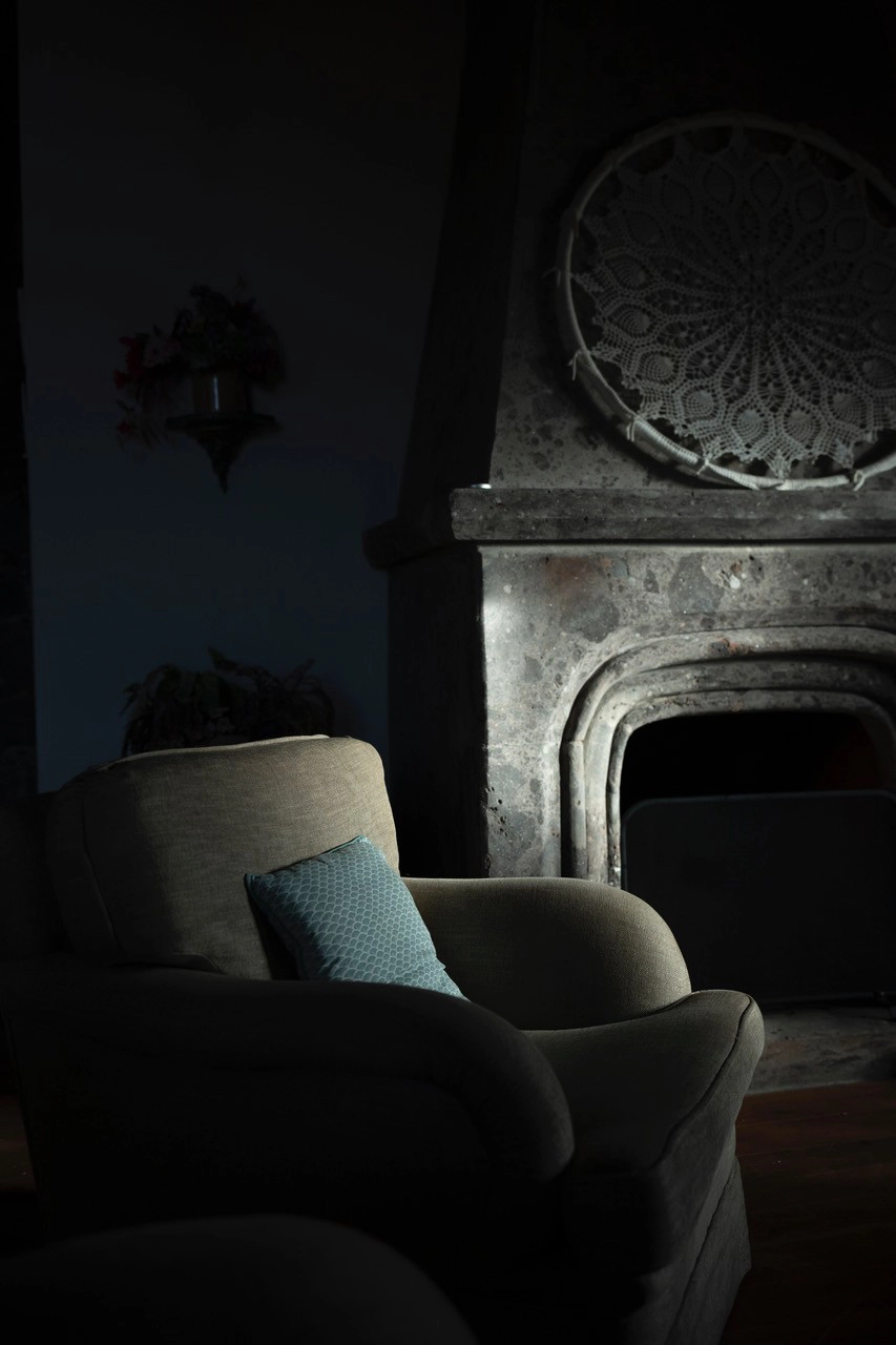 A quiet living room scene with a stone fireplace and soft morning light on an empty armchair—illustrating the atmospheric setup used when photographing portraits in early morning light.