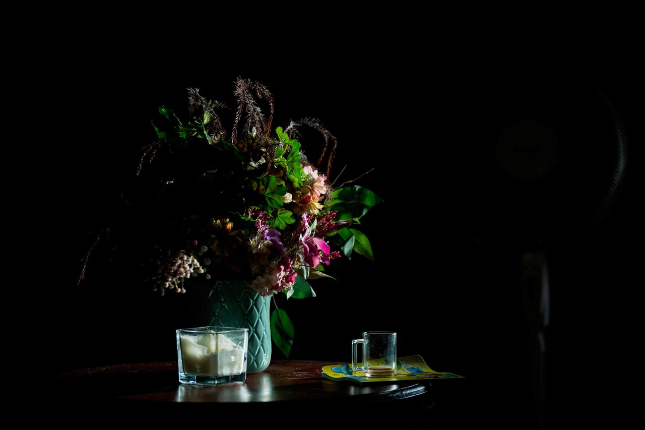 A still life of a flower arrangement and glassware dramatically lit by a beam of morning sunlight—showcasing the type of natural light used when photographing portraits in early morning light.