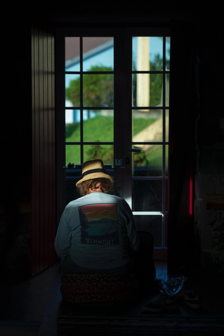 A person seated inside, facing a sunlit window with a clear view outdoors—illustrating balanced exposure and natural backlighting when photographing portraits in early morning light.