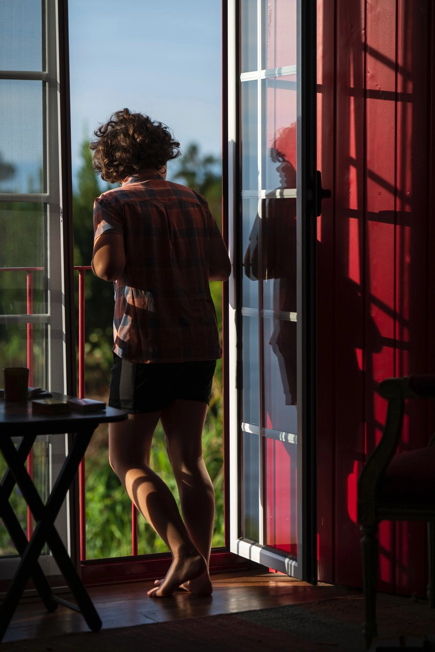 A child standing barefoot in the warm glow of early morning sun at an open doorway—capturing the fleeting quality of natural light when photographing portraits in early morning light.