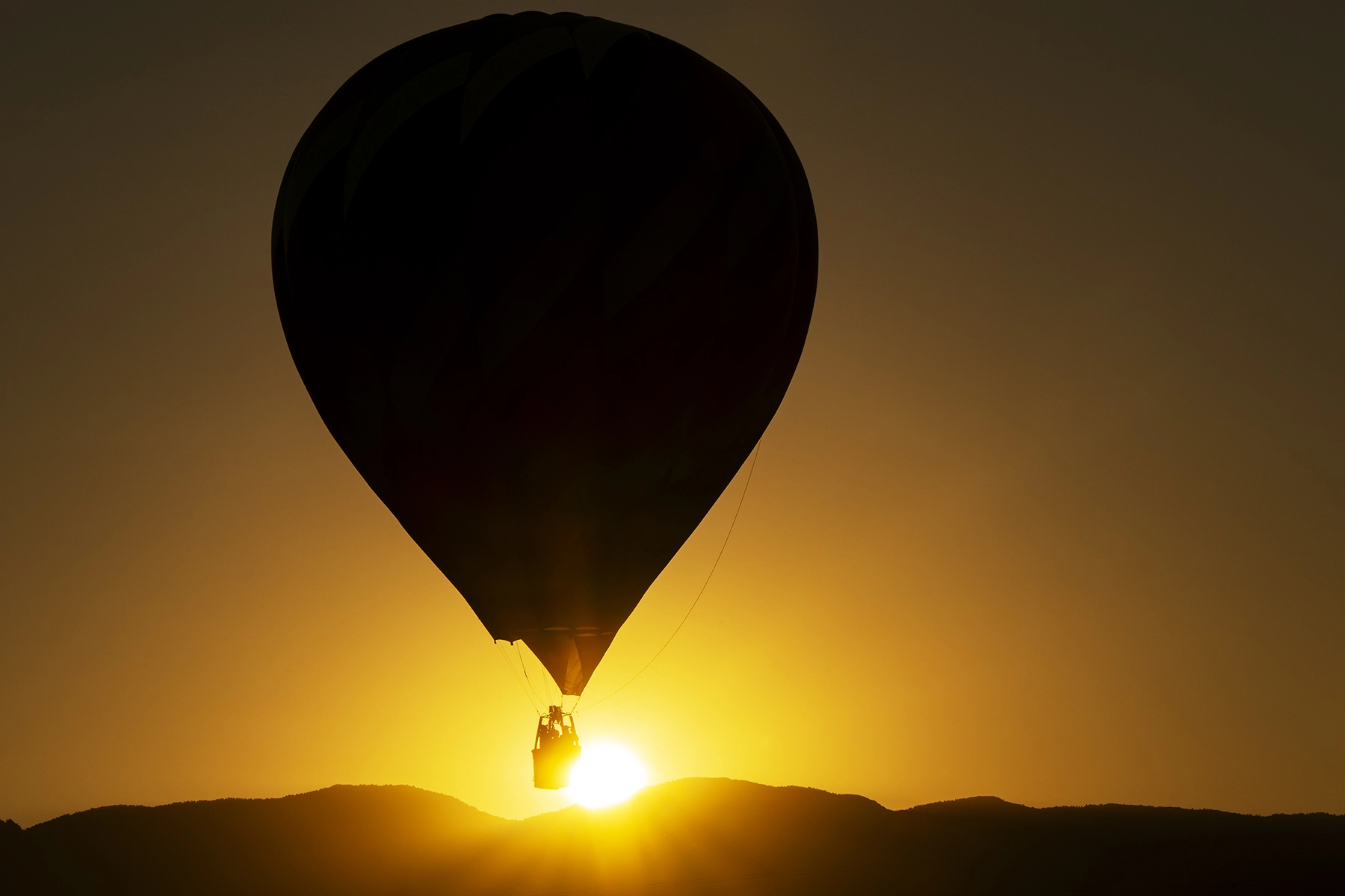 Silhouette of a hot air balloon floating above mountain peaks against a golden sunrise sky.