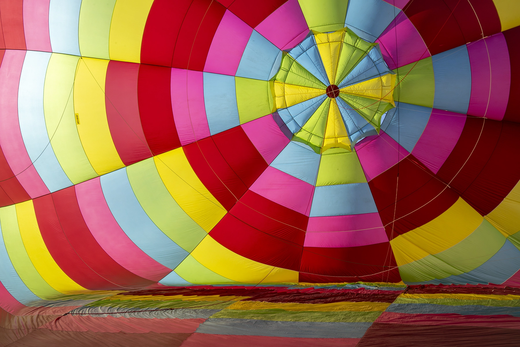Vibrant interior view of a partially inflated hot air balloon, showcasing colorful fabric panels in red, yellow, blue, green, and pink.