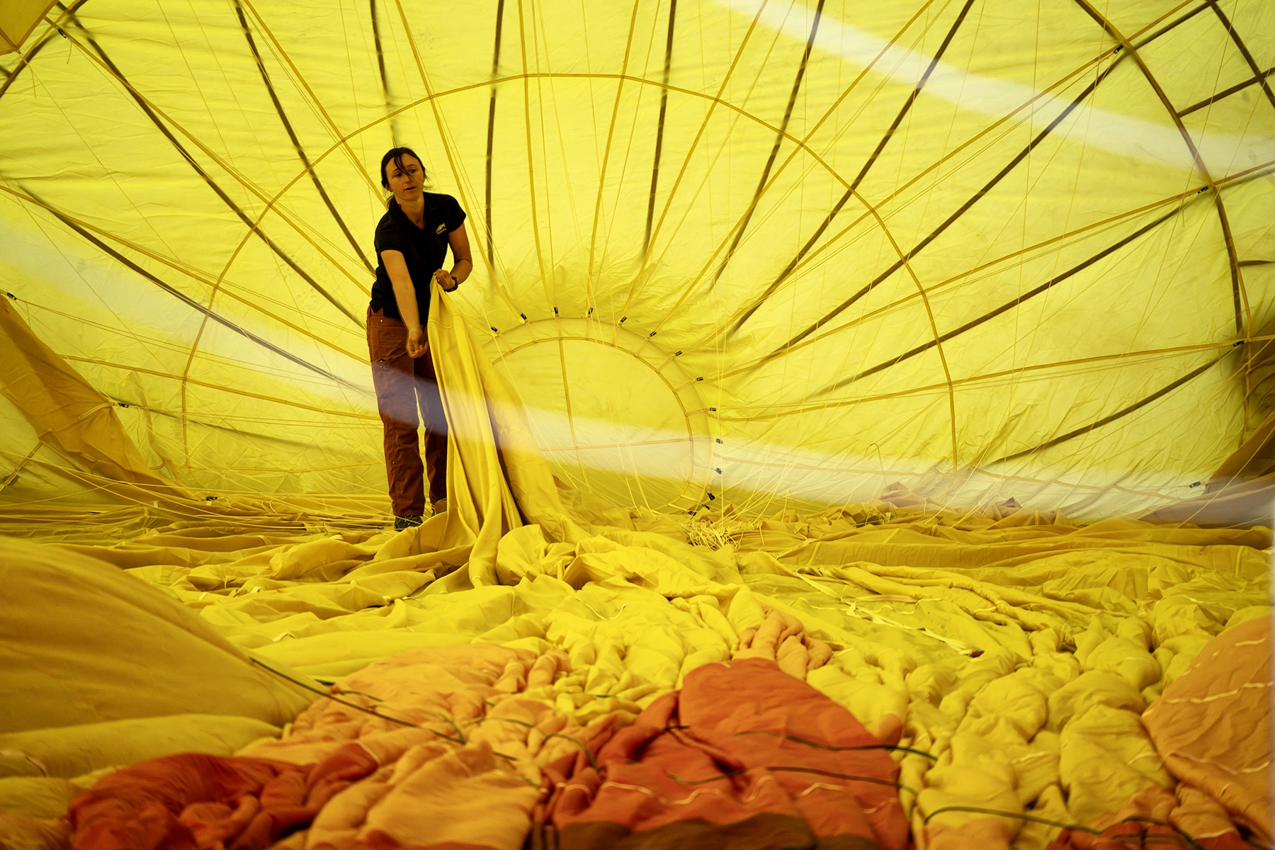 Person inside a partially inflated yellow hot air balloon, adjusting the fabric during the preparation process at a balloon festival.