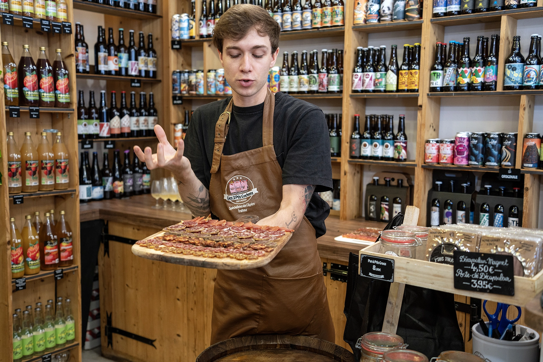A shop attendant presenting a tray of cured meats in a specialty food and beverage store.