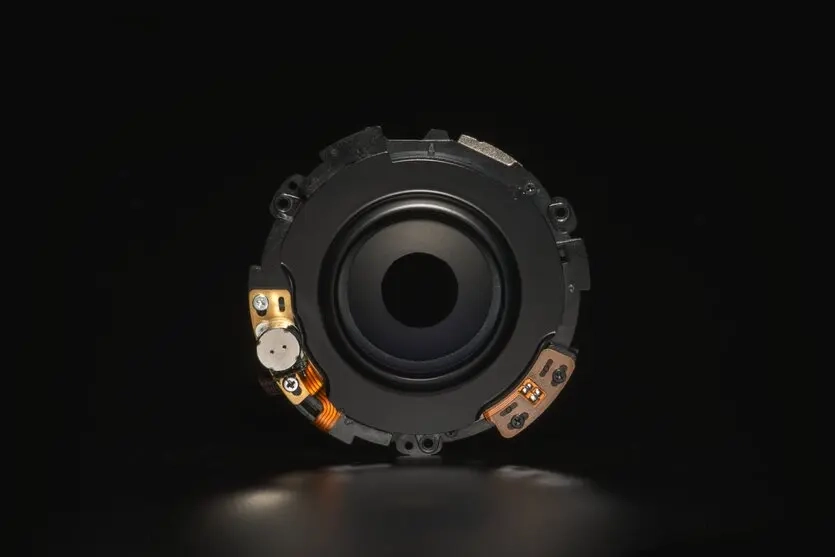 Internal view of a camera lens aperture mechanism showing the circular diaphragm blades and electronic components used to control light entry.