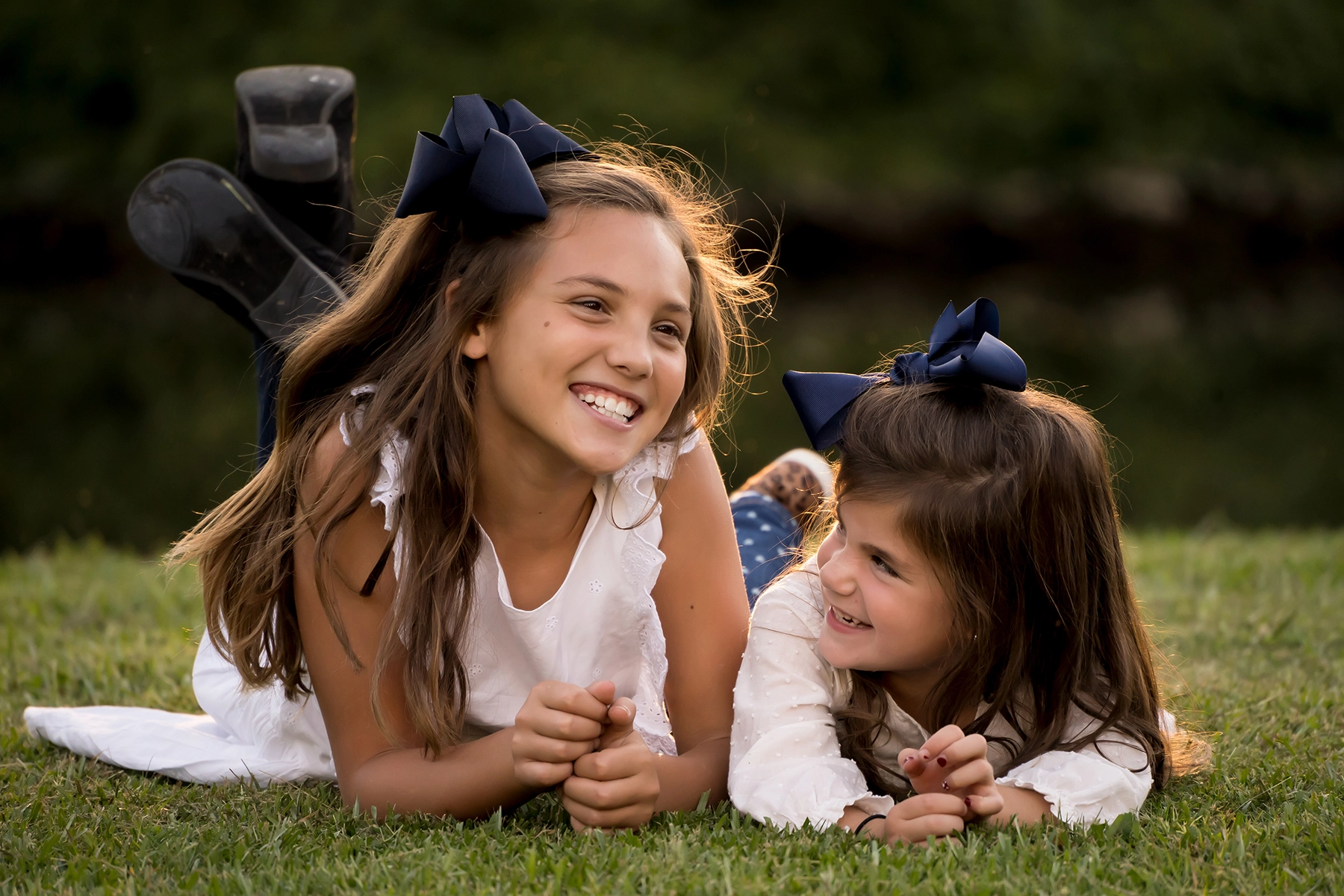 Two smiling young girls lying on grass in warm sunlight.