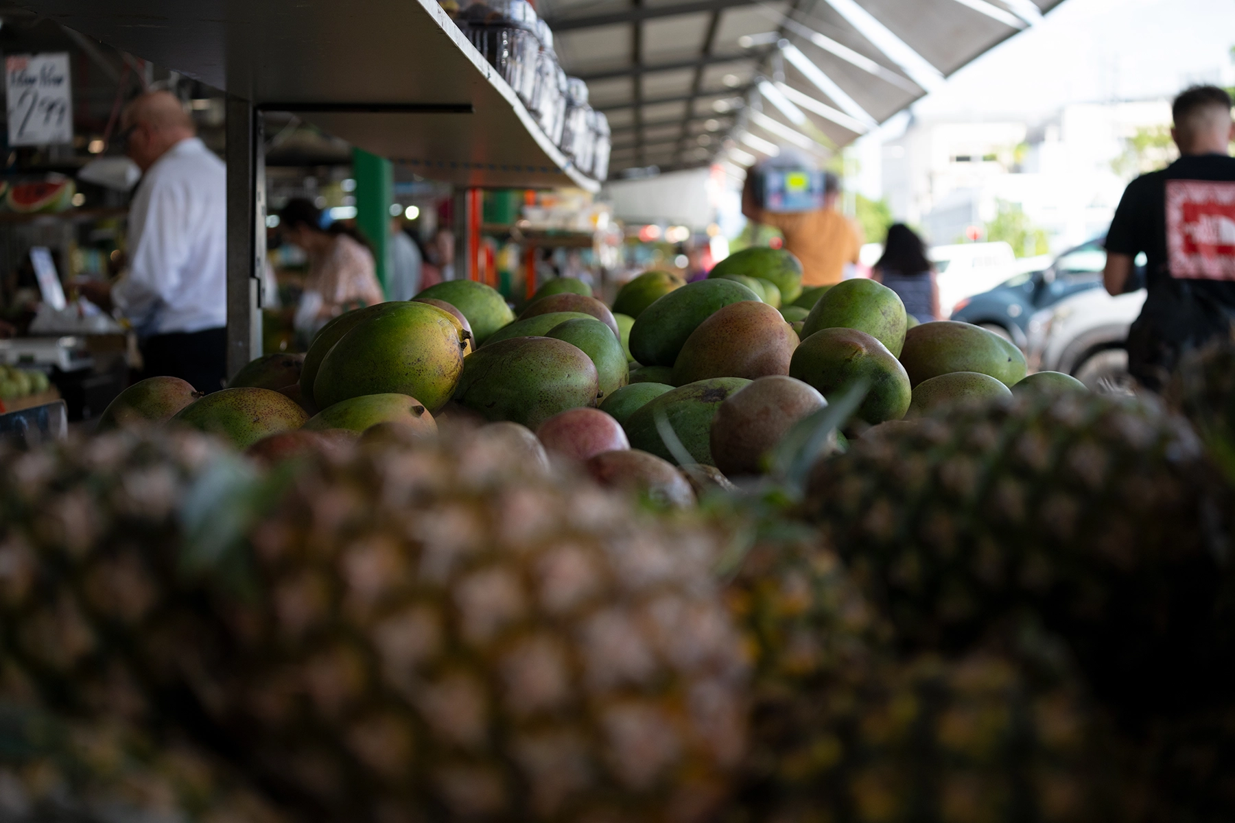 Outdoor market scene with sharp-focus mangoes at center and pineapples in the foreground blurred by soft bokeh.