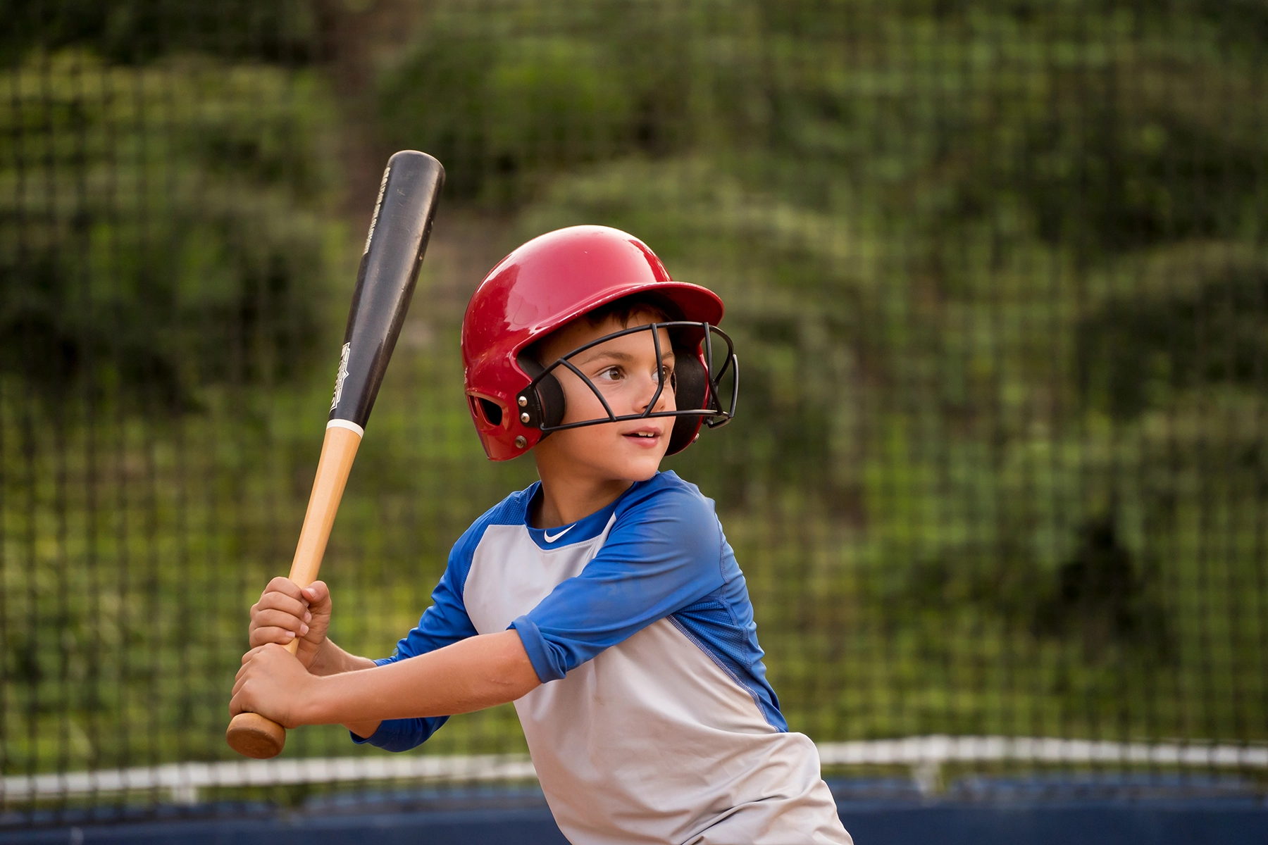 Young boy in a red helmet preparing to bat during a baseball game, captured with a telephoto lens to highlight facial expression and isolate the subject from the background.