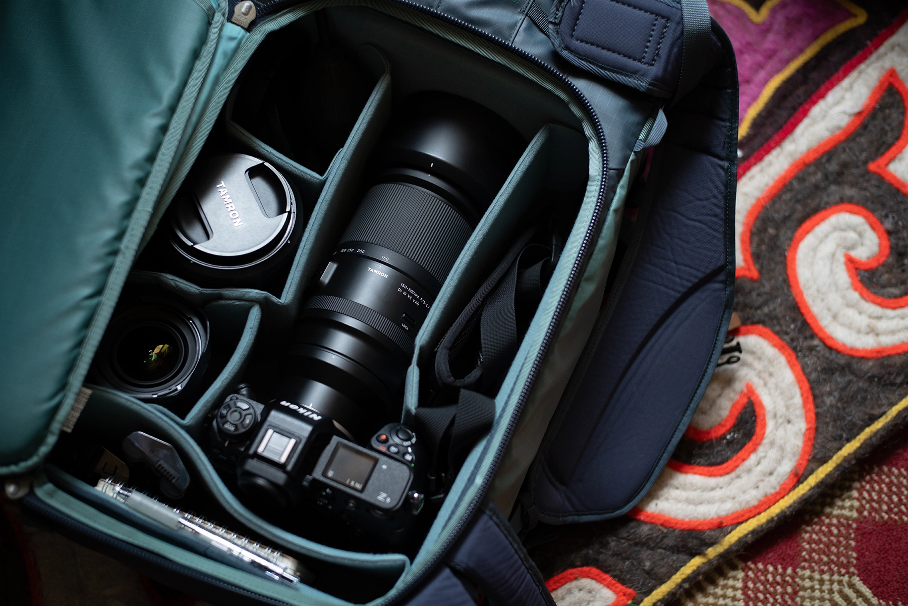 Camera backpack neatly packed with Tamron telephoto lens, mirrorless camera, and accessories, ready for on-the-go photography.