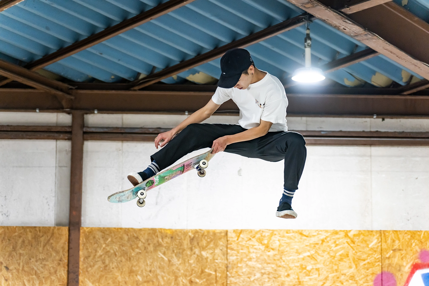 Skateboarder mid-air during an indoor trick, captured at a medium telephoto focal length to freeze motion and emphasize subject clarity under artificial lighting.