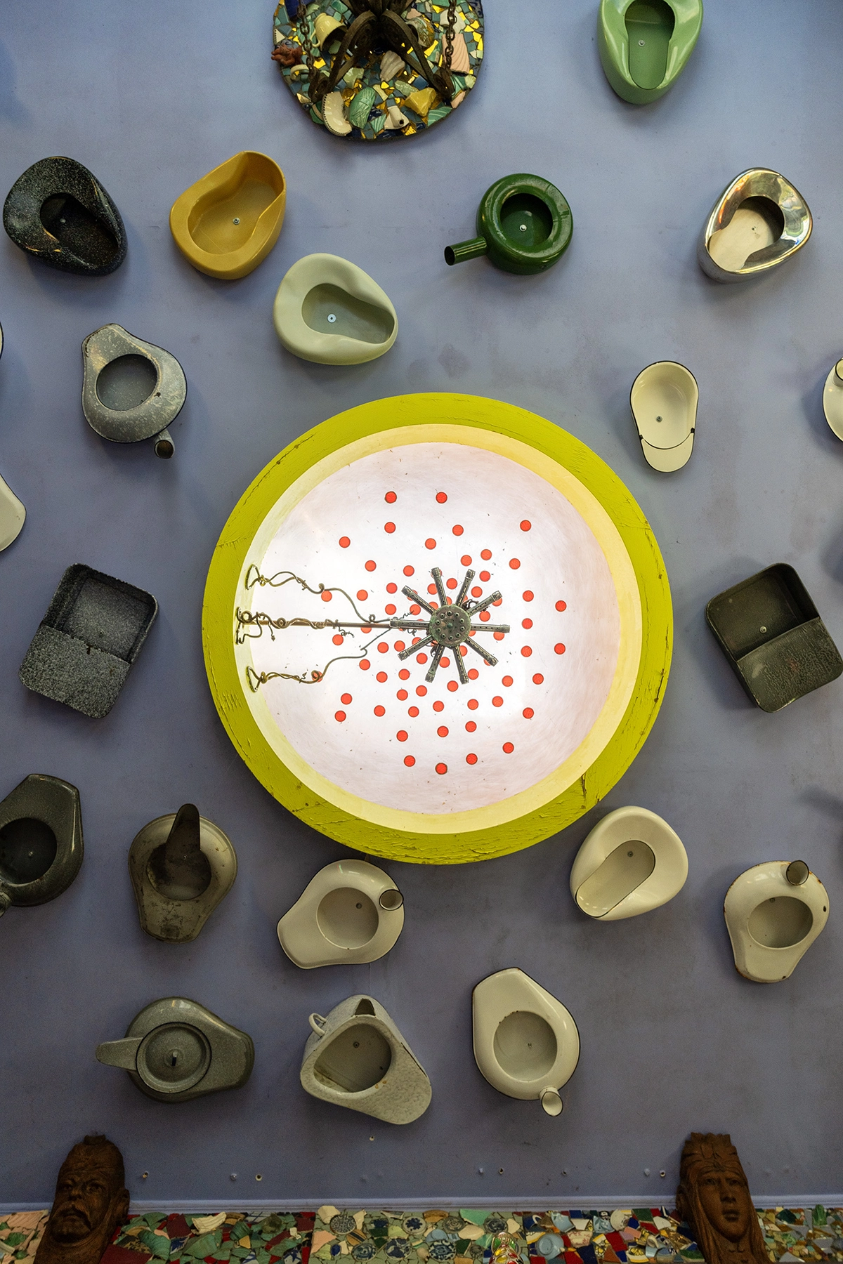 Overhead view of a surreal art installation at Luna Parc featuring vintage urinals, teapots, and a brightly lit circular chandelier with red dots—an example of photographing unconventional subjects and abstract art in interior spaces.
