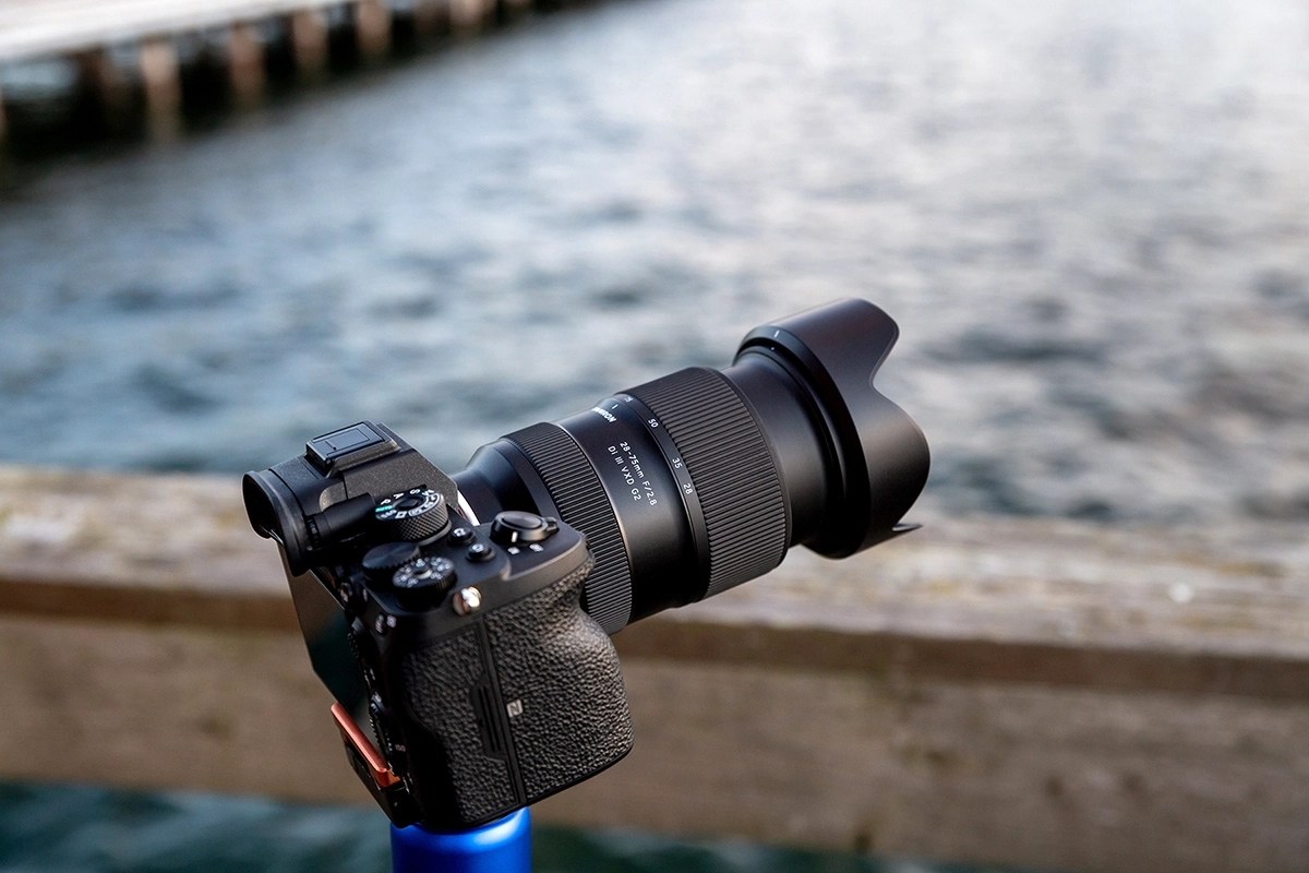 Una cámara sin espejo montada con un objetivo Tamron sobre un trípode, capturando imágenes estables frente al mar: un ejemplo de los principios básicos del trabajo de cámara para la grabación de vídeo.