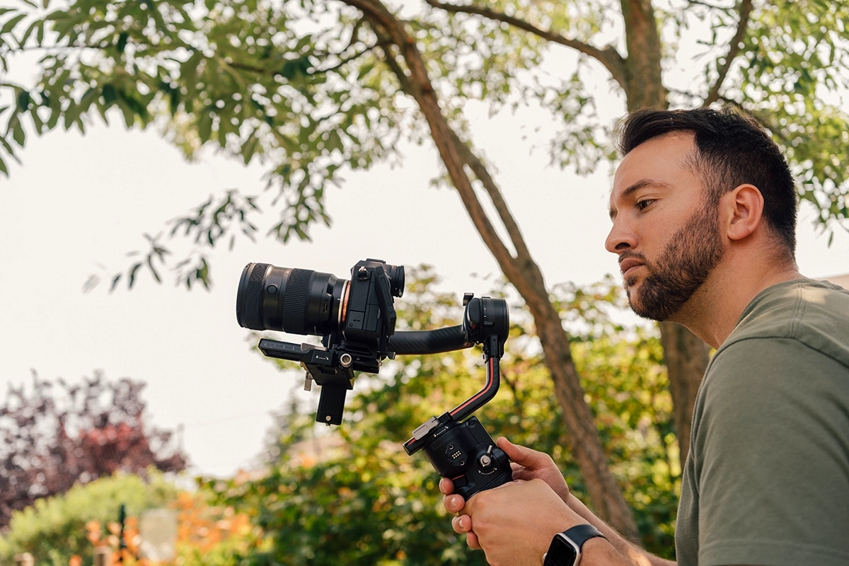 Un camarógrafo utiliza una cámara sin espejo montada sobre cardán en exteriores para demostrar los aspectos básicos de la grabación de vídeo con seguimiento suave.