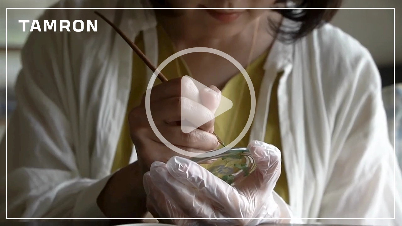 Primer plano de una mujer pintando cuidadosamente cristalería a mano con guantes, destacando la artesanía y la atención a los detalles visuales.