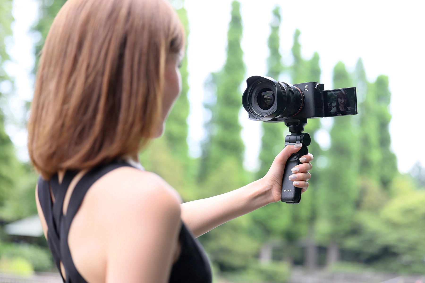 Mulher fazendo um vlog ao ar livre usando uma câmera sem espelho com uma tela flip montada em um tripé de mão.